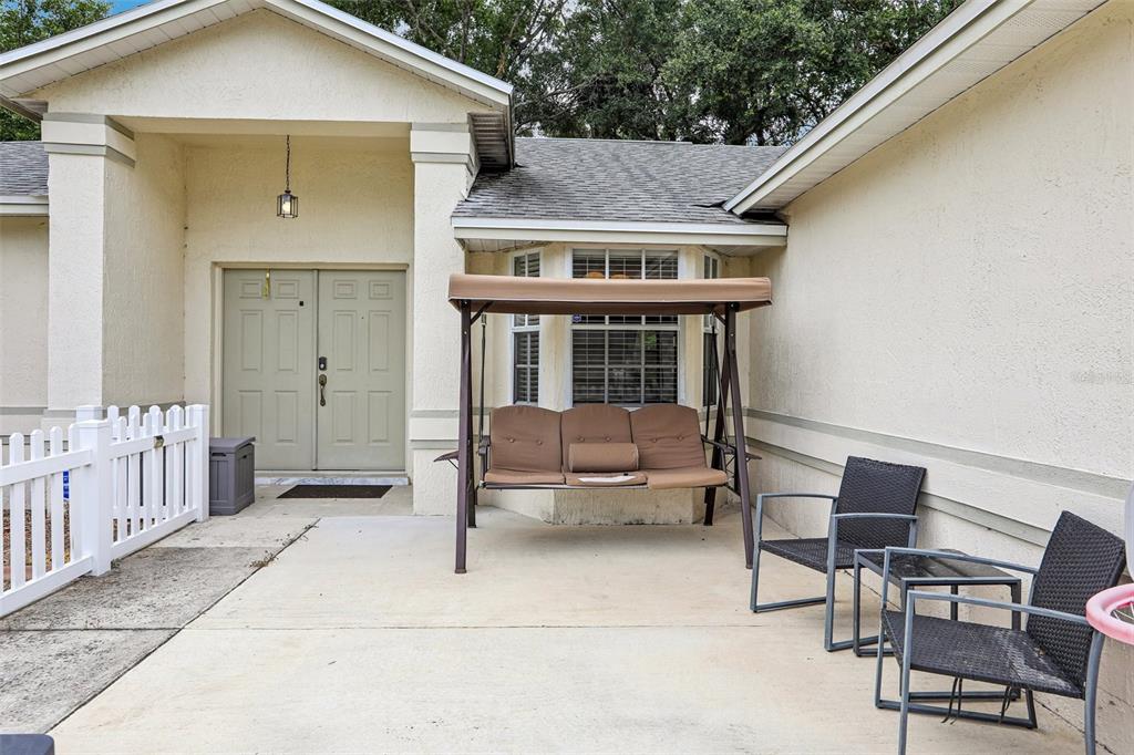 A concrete patio features a porch swing and two chairs in front of a house entrance — 3434 DIAMOND TERRACE, MULBERRY, FL