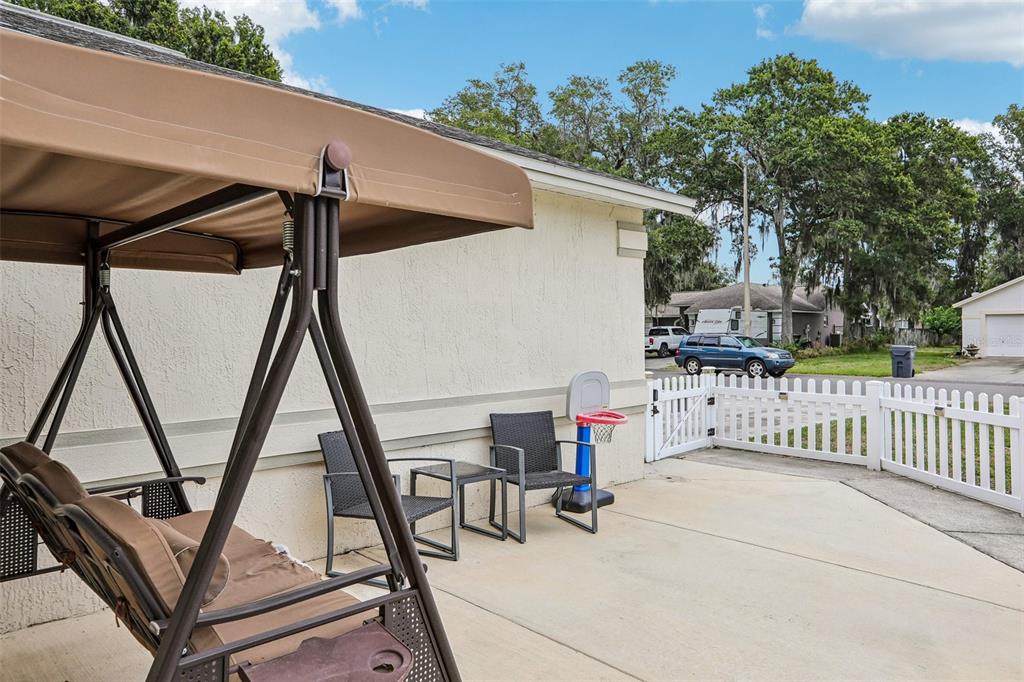 A patio features a brown porch swing, two chairs, a small table, and a basketball hoop — 3434 DIAMOND TERRACE, MULBERRY, FL
