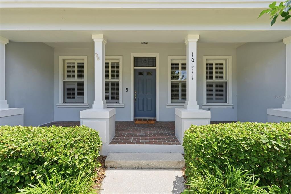 A front porch with a blue door, brick flooring, and two white columns — 10111 HAYFIELD WAY, TAMPA, FL