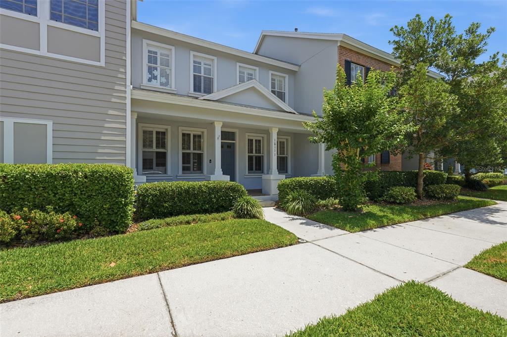 A two-story townhouse exterior features light gray siding, a covered front porch, and manicured hedges — 10111 HAYFIELD WAY, TAMPA, FL