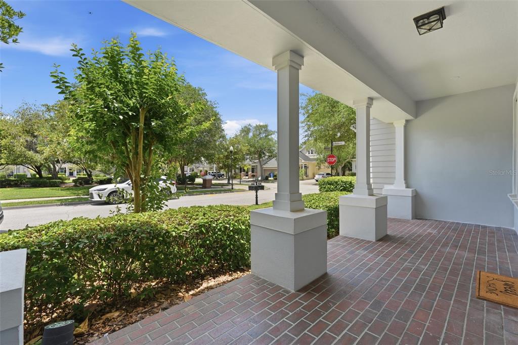 A covered front porch with brick flooring, white columns, and a view of the street — 10111 HAYFIELD WAY, TAMPA, FL