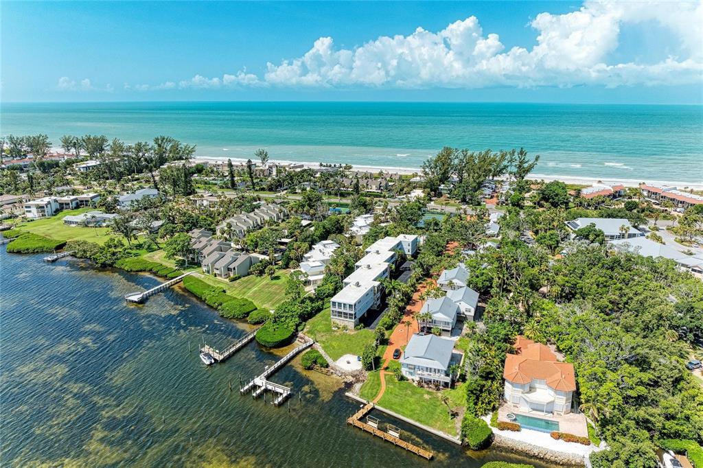 An aerial view shows waterfront residential buildings, private docks, and a beach along the ocean — 5320 GULF OF MEXICO DRIVE UNIT 204, LONGBOAT KEY, FL