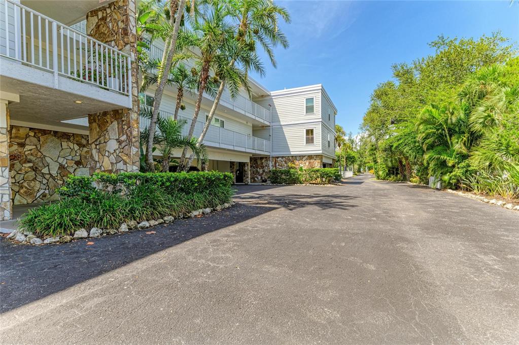 A multi-story apartment building with stone accents and palm trees sits beside a paved driveway — 5320 GULF OF MEXICO DRIVE UNIT 204, LONGBOAT KEY, FL