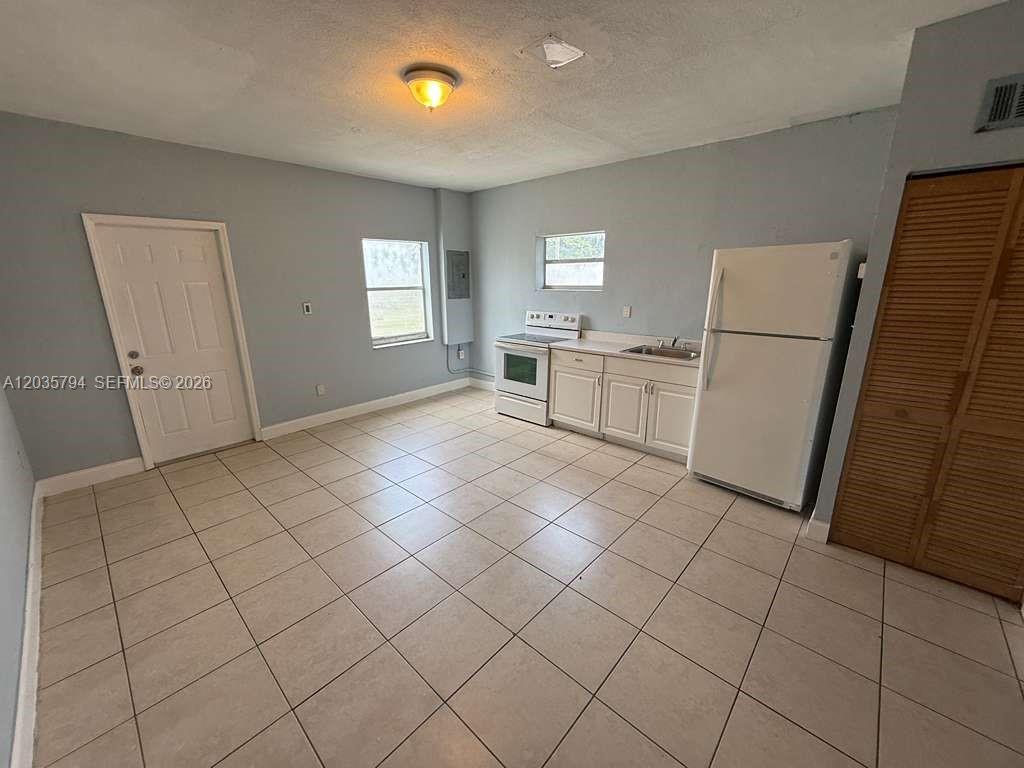 This kitchen features white cabinets, a white refrigerator, a stove, and light-colored floor tiles — 2014 Funston St # C, Hollywood FL 33020, HOLLYWOOD, FL