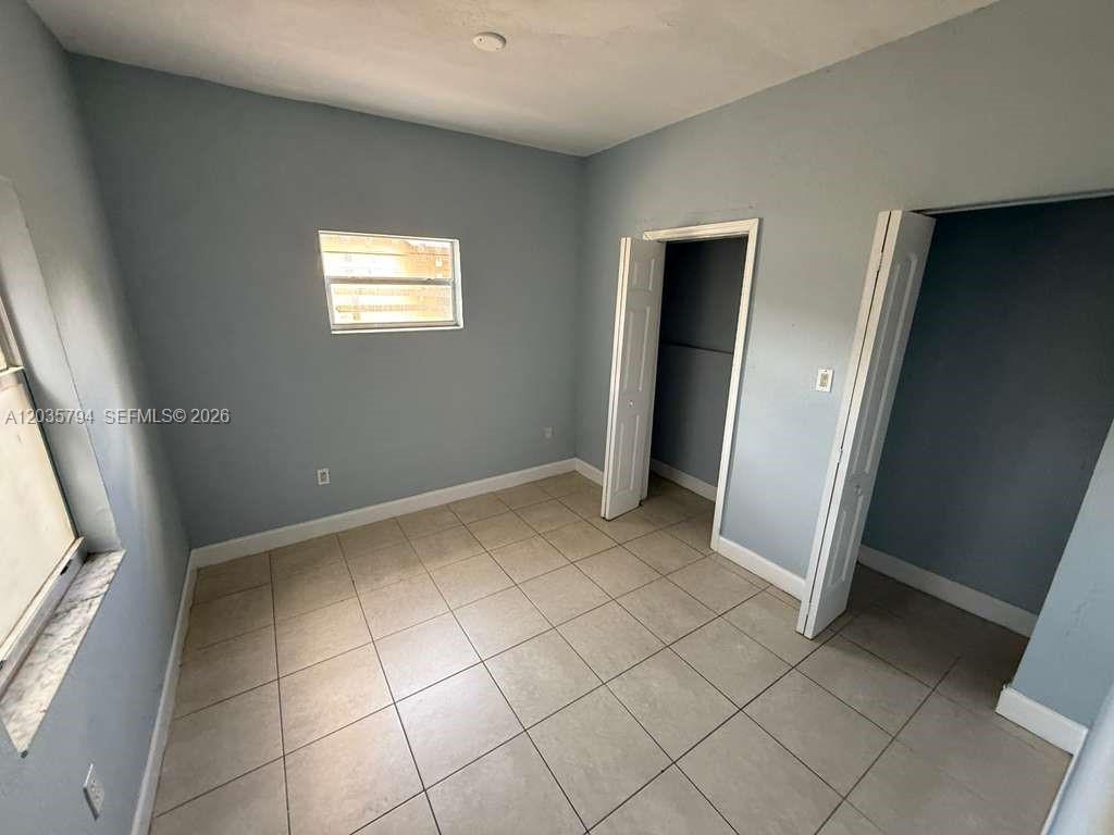 An empty bedroom with light blue walls, beige tile flooring, and a small closet — 2014 Funston St # C, Hollywood FL 33020, HOLLYWOOD, FL