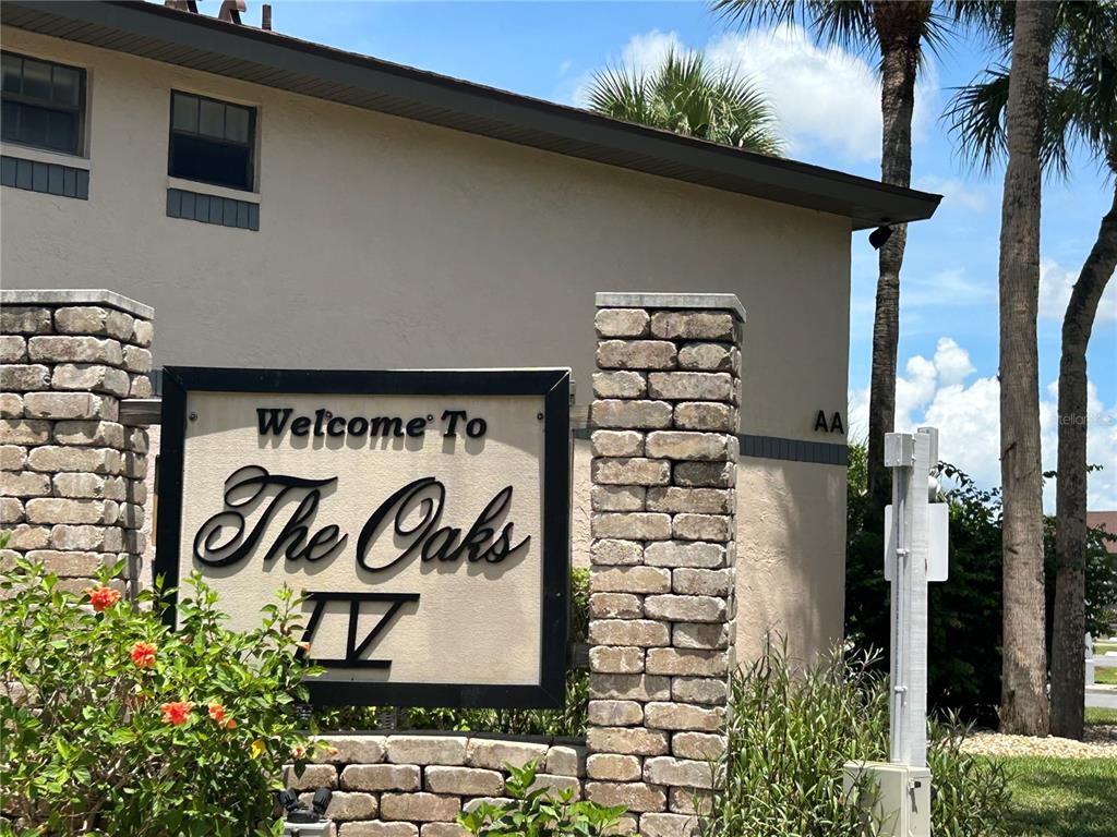 A sign reading Welcome To The Oaks IV stands in front of a tan building — 19505 QUESADA AVENUE UNIT AA201, PORT CHARLOTTE, FL