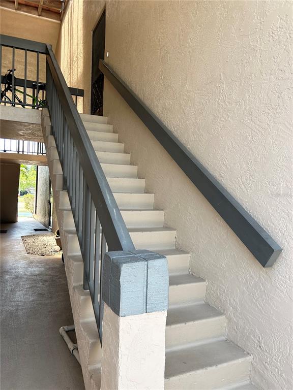 An outdoor staircase with gray railings leads to an upper-level entrance against a beige wall — 19505 QUESADA AVENUE UNIT AA201, PORT CHARLOTTE, FL