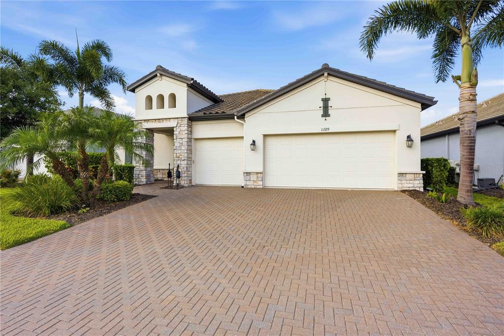 A single-story house with a paved driveway, three-car garage, and palm trees in the front yard — 11329 MONTSERRAT DRIVE, VENICE, FL