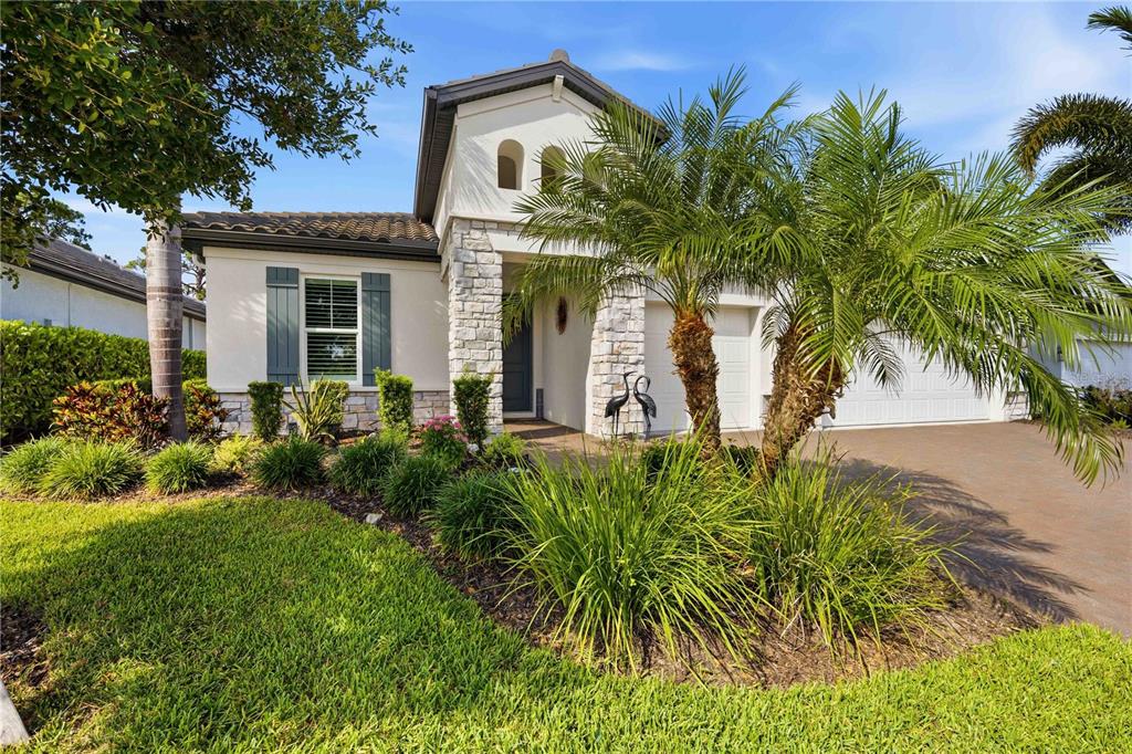 A single-story house with a stone facade, palm trees, and a paved driveway — 11329 MONTSERRAT DRIVE, VENICE, FL