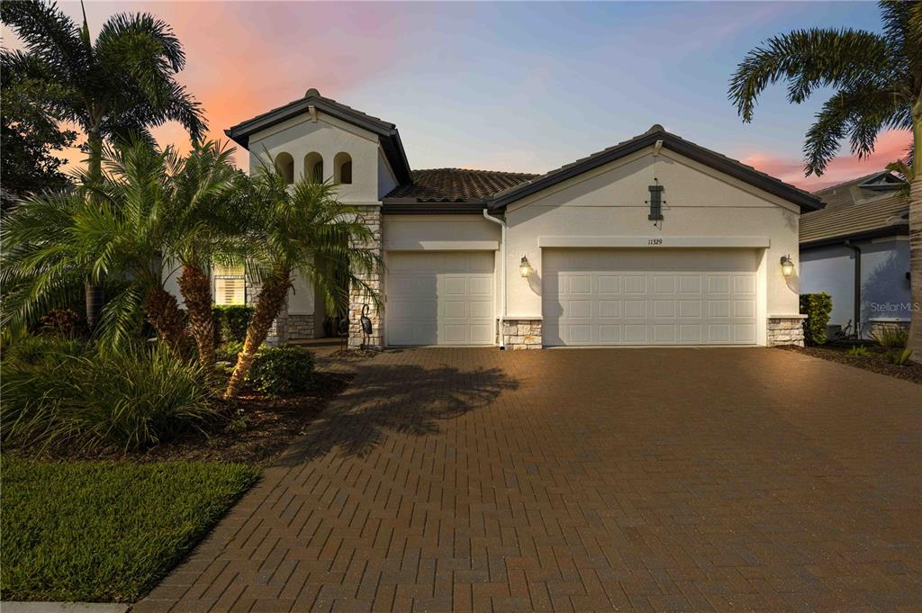 A single-story house with a paved driveway, two-car garage, and palm trees at sunset — 11329 MONTSERRAT DRIVE, VENICE, FL