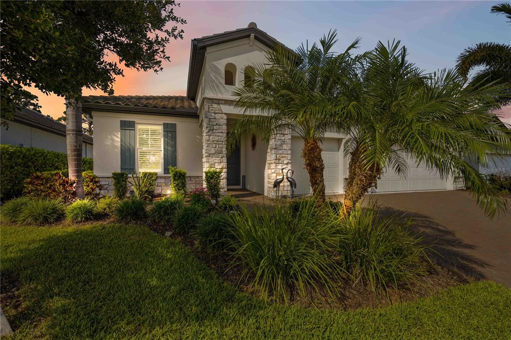 A single-story house with a stone facade, palm trees, and a driveway at sunset — 11329 MONTSERRAT DRIVE, VENICE, FL