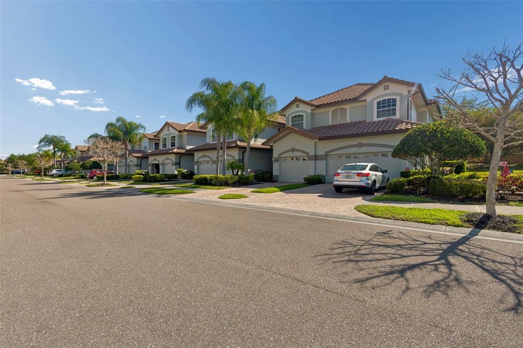 A street-level view of suburban houses with tile roofs, palm trees, and a parked car — 8235 MIRAMAR WAY, LAKEWOOD RANCH, FL