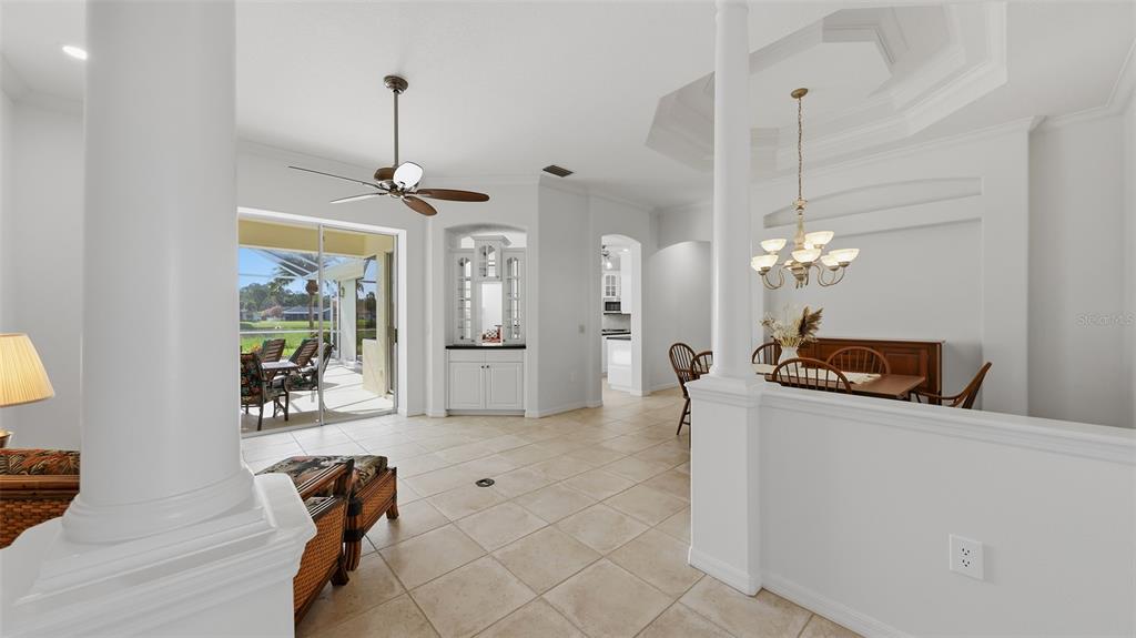 A bright, open-concept living and dining area features tile floors, white columns, and sliding glass doors — 6228 AVENTURA DRIVE, SARASOTA, FL