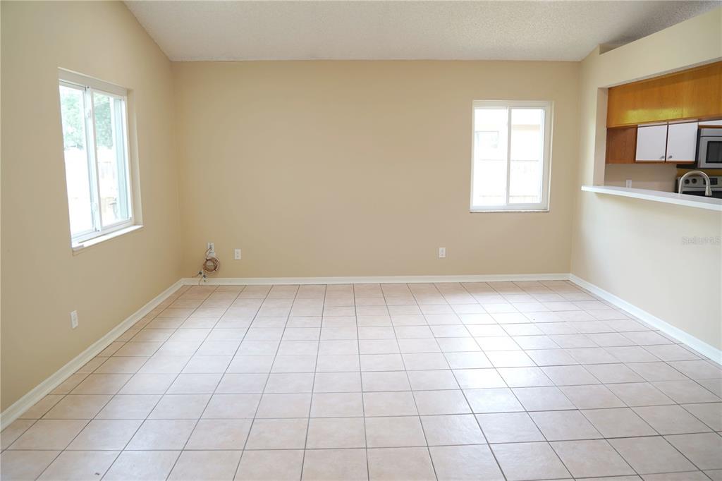 An empty living room features beige walls, tile flooring, two windows, and a kitchen pass-through — 4304 BARRET AVENUE, PLANT CITY, FL