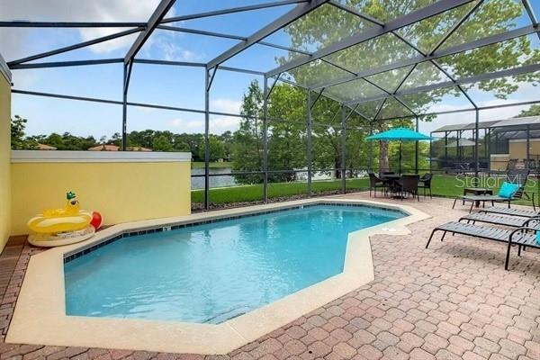 A screened-in swimming pool with a patio and outdoor furniture overlooks a lake — 3163 YELLOW LANTANA LANE, KISSIMMEE, FL