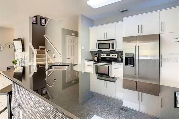 A modern kitchen features white cabinetry, stainless steel appliances, and a dark granite island countertop — 3163 YELLOW LANTANA LANE, KISSIMMEE, FL
