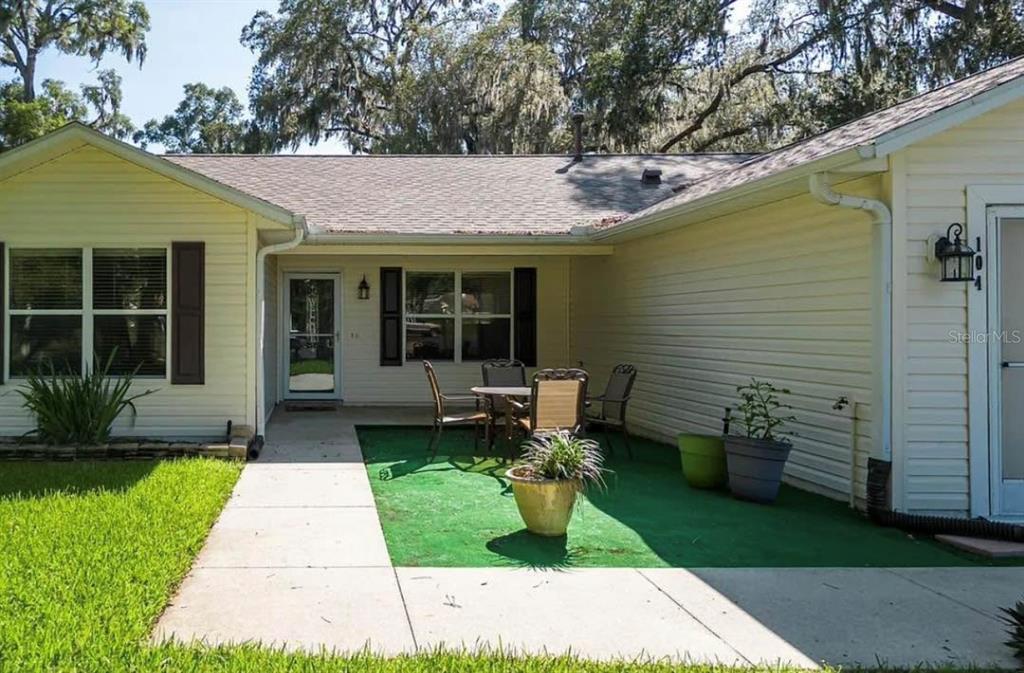 A yellow house exterior features a concrete walkway leading to a patio with green turf — 104 CHERRY BLOSSOM LANE, LADY LAKE, FL