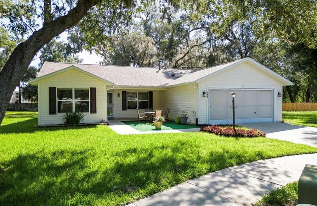 A single-story house with light siding, a two-car garage, and a small front patio area — 104 CHERRY BLOSSOM LANE, LADY LAKE, FL