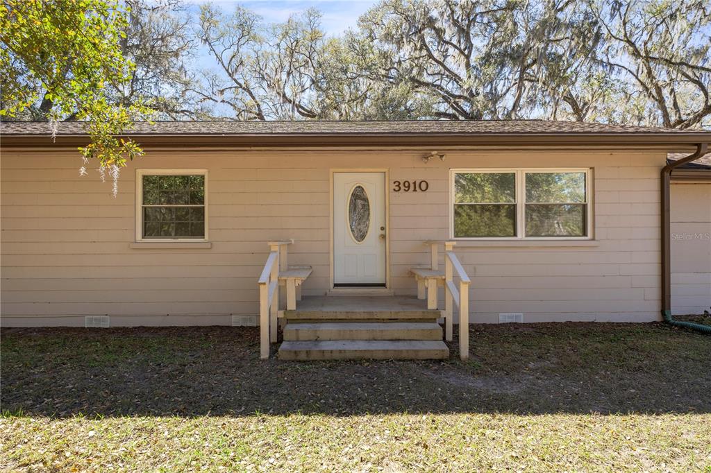 A single-story house exterior features beige horizontal siding, a white front door, and concrete steps — 3910 SE 52ND STREET, OCALA, FL