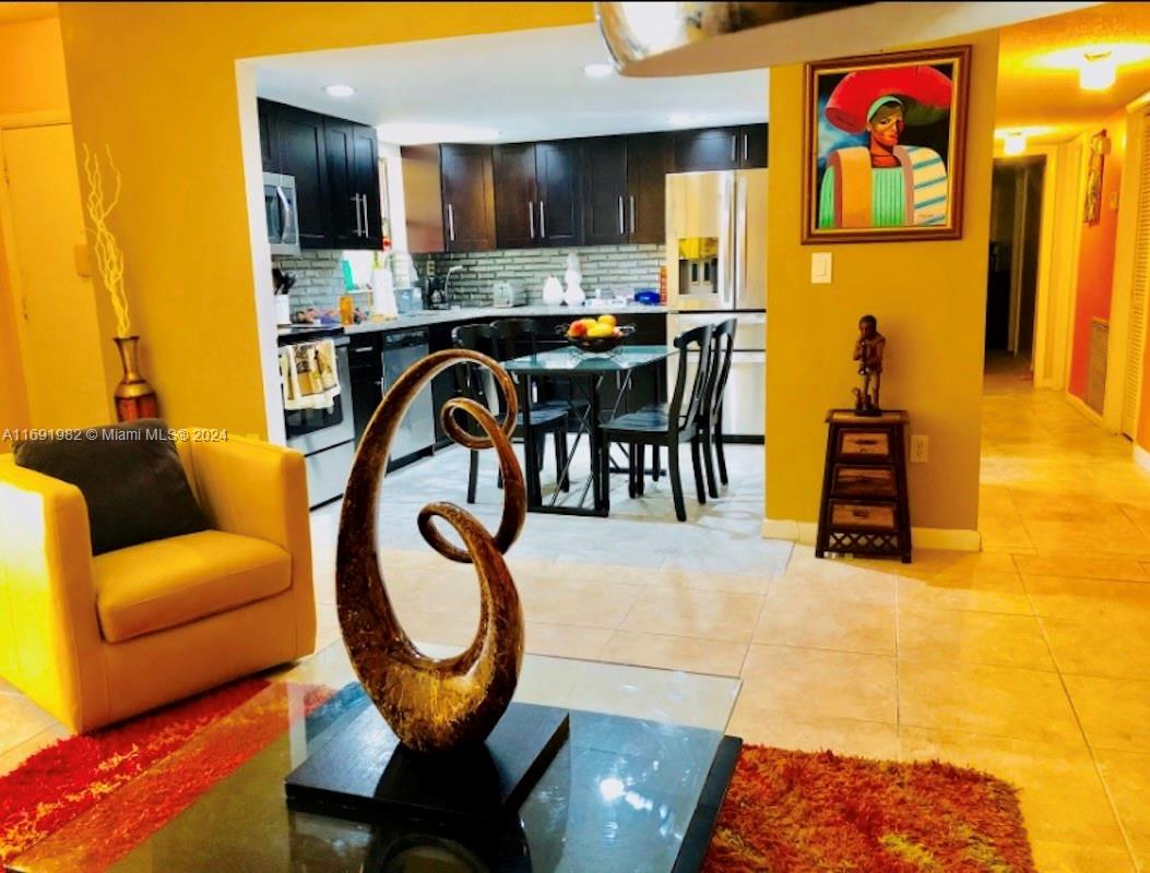 A living room with a yellow armchair leads into a kitchen with dark cabinetry — 740 NE 199th St # 206G, Miami FL 33179, MIAMI, FL