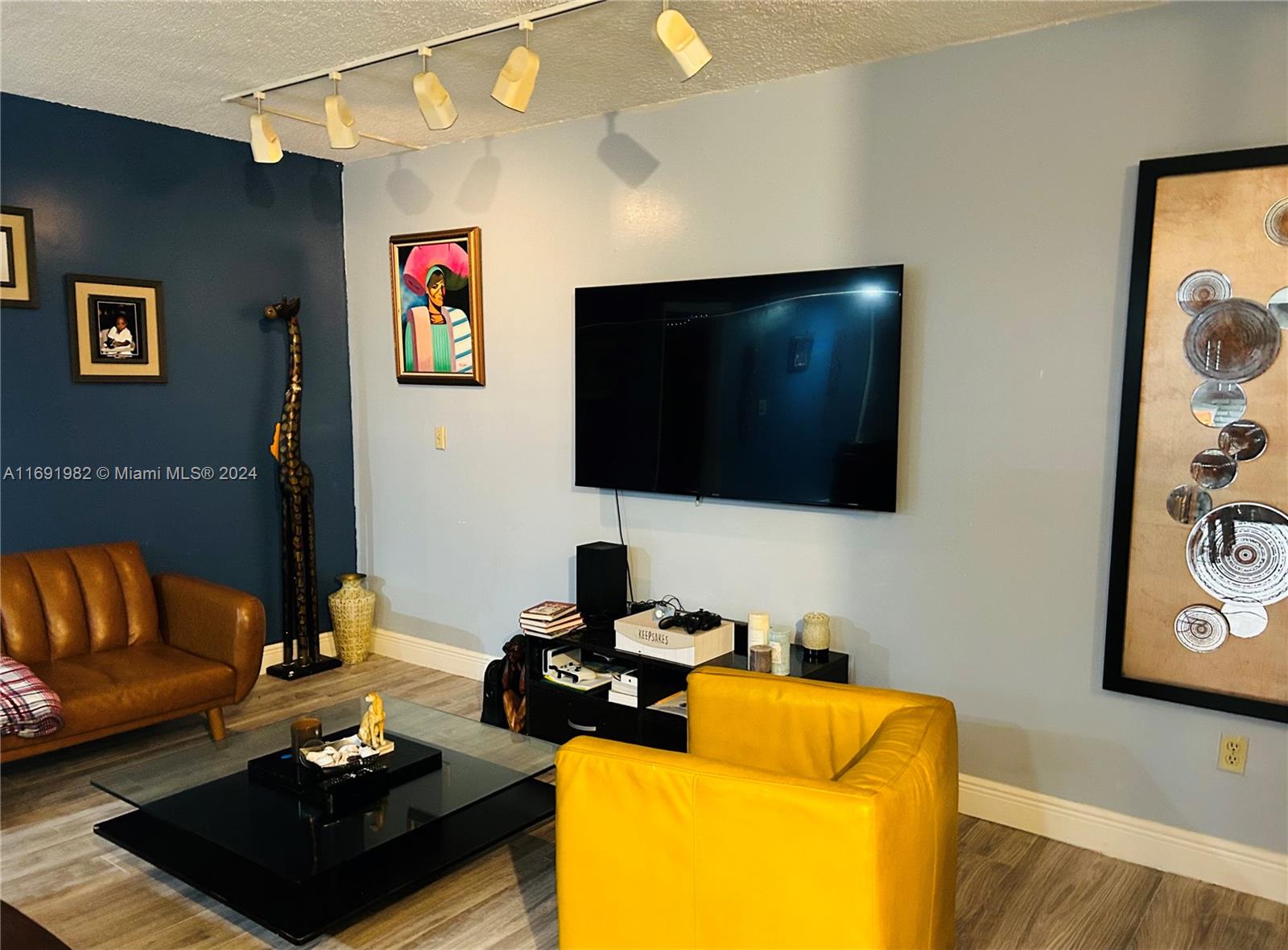 A living room features a mounted television, a brown sofa, and a yellow armchair — 740 NE 199th St # 206G, Miami FL 33179, MIAMI, FL
