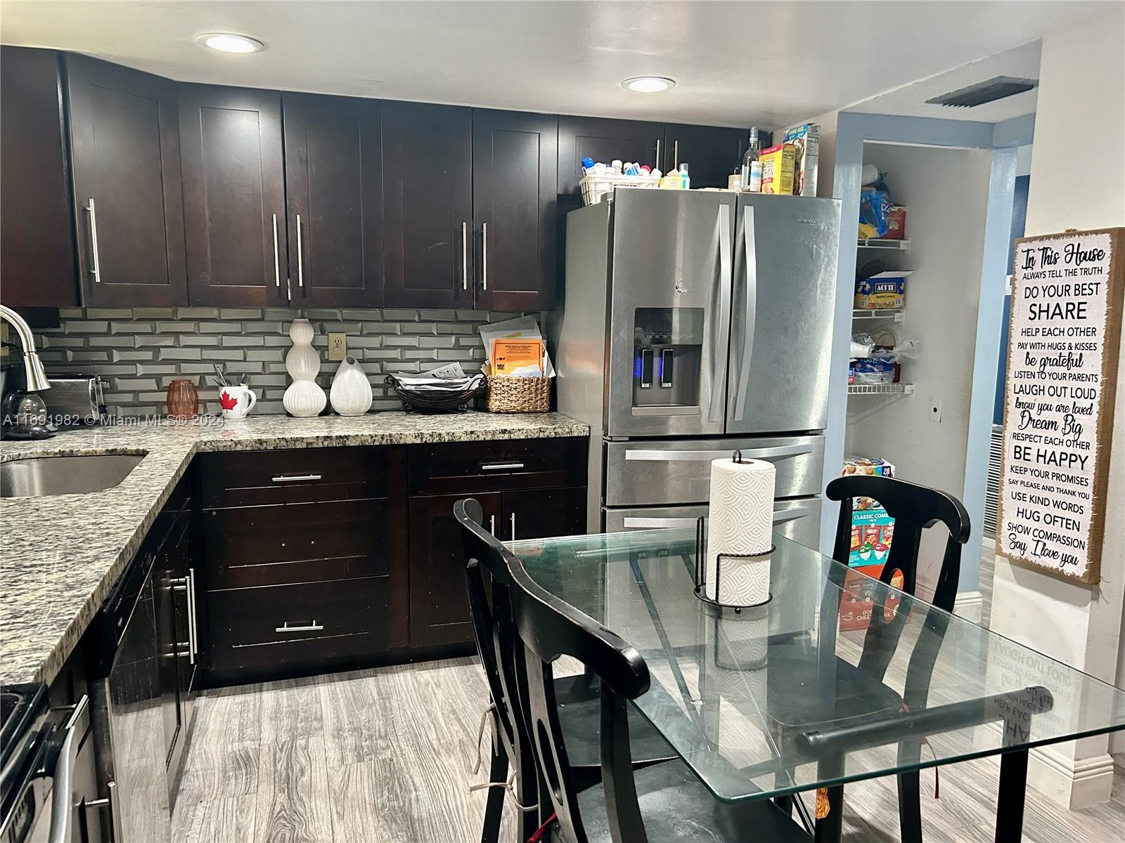 A kitchen features dark wood cabinets, granite countertops, stainless steel appliances, and a glass dining table — 740 NE 199th St # 206G, Miami FL 33179, MIAMI, FL