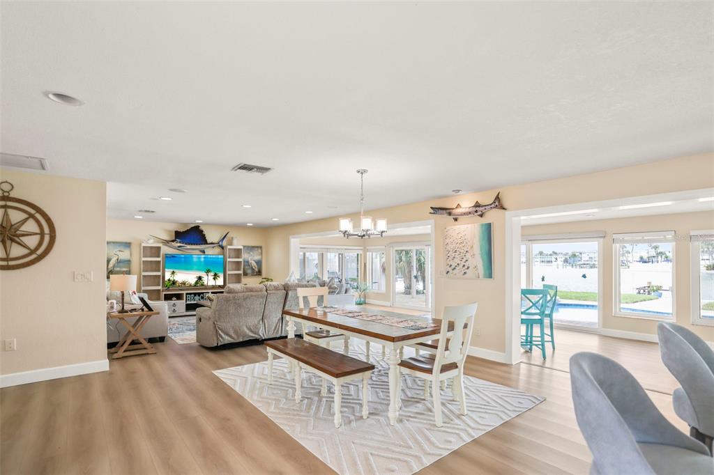 An open-concept living and dining area with light wood flooring and views of a pool — 6360 2ND PALM POINT, ST PETERSBURG, FL