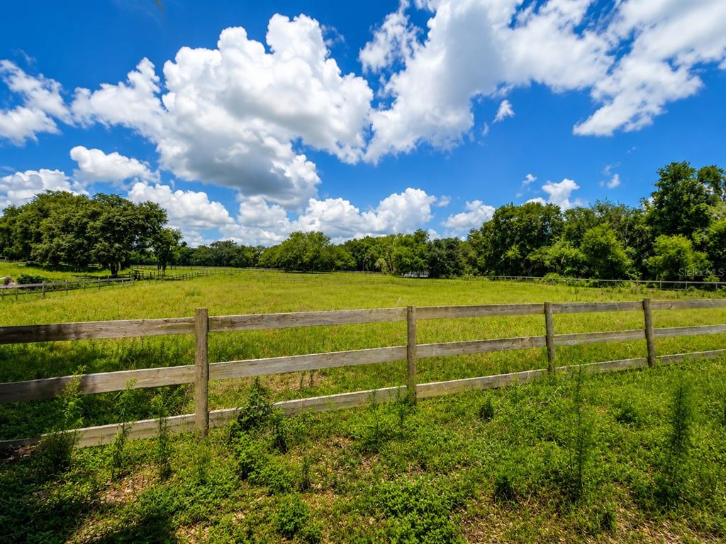 A wooden porch with chairs overlooks a grassy yard and a red barn — 13691 S HWY 25, EASTLAKE WEIR, FL