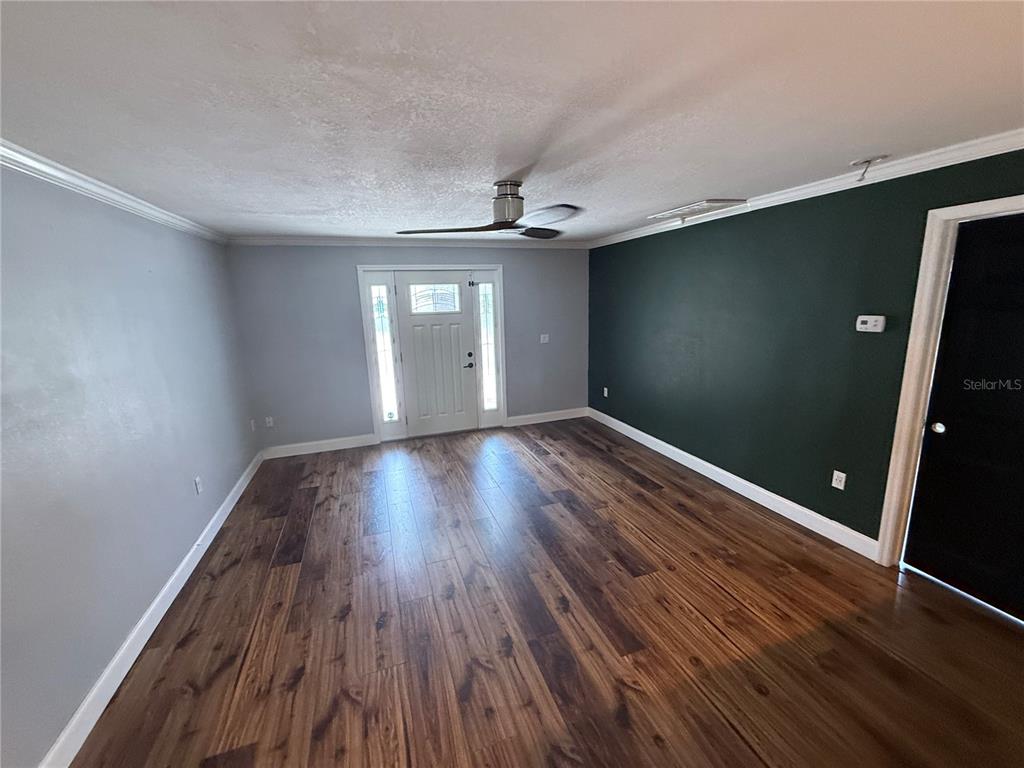 A living room features dark wood-look flooring, light gray walls, and a dark green accent wall — 2722 9TH AVENUE W, BRADENTON, FL