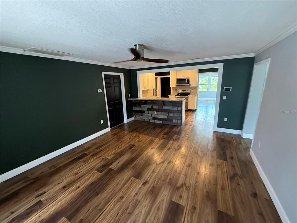 A living room with dark green walls, wood-look flooring, and a kitchen pass-through with stone — 2722 9TH AVENUE W, BRADENTON, FL