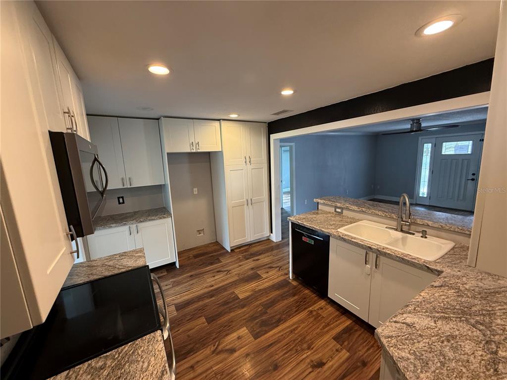 A kitchen features white cabinetry, granite countertops, stainless steel appliances, and dark wood-look flooring — 2722 9TH AVENUE W, BRADENTON, FL