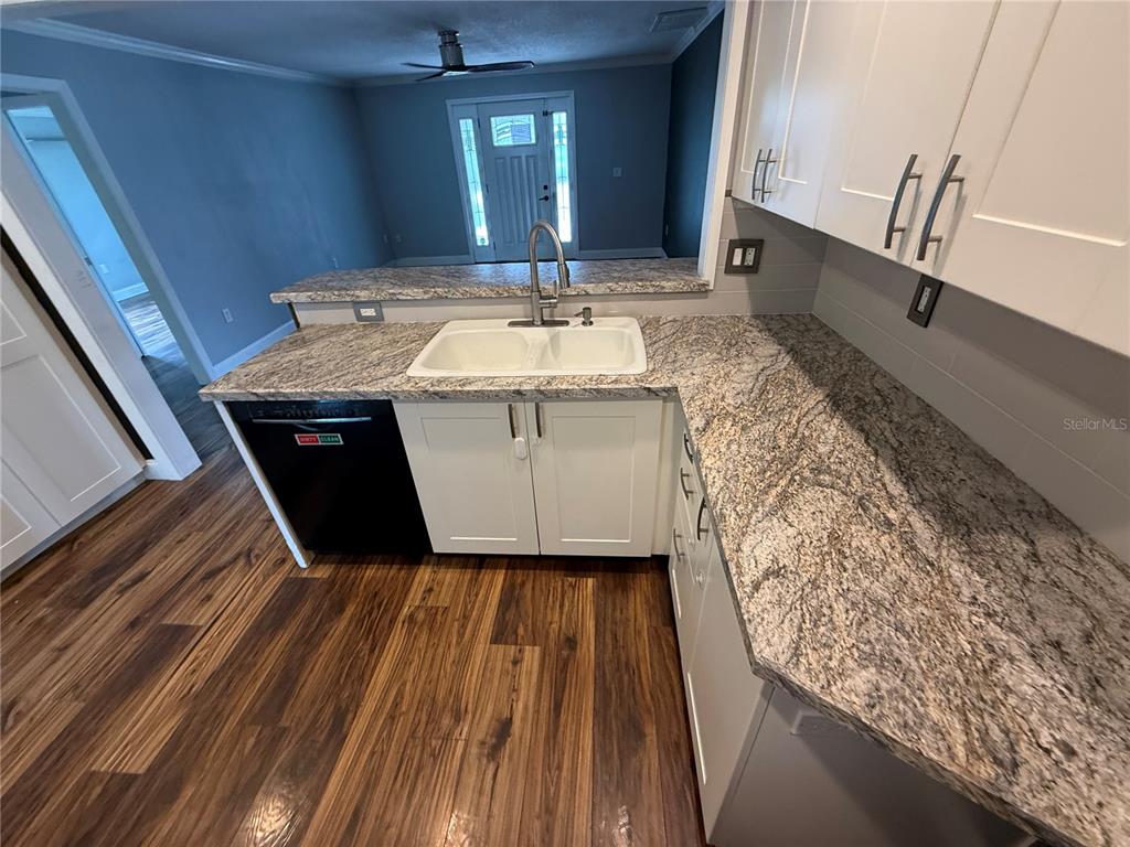 A kitchen features white cabinets, granite countertops, a double sink, and dark wood flooring — 2722 9TH AVENUE W, BRADENTON, FL