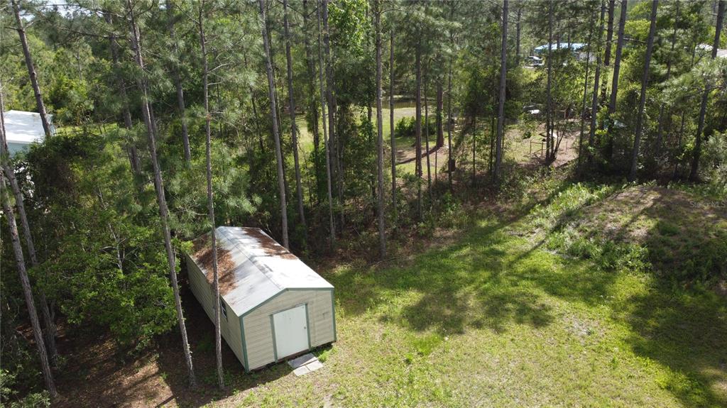 An aerial view shows a small storage shed situated in a wooded, grassy backyard — 10205 BAYLOR AVENUE, HASTINGS, FL