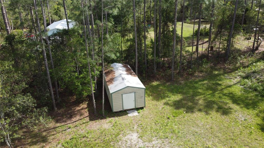An aerial view shows a rectangular storage shed situated in a wooded, grassy yard — 10205 BAYLOR AVENUE, HASTINGS, FL