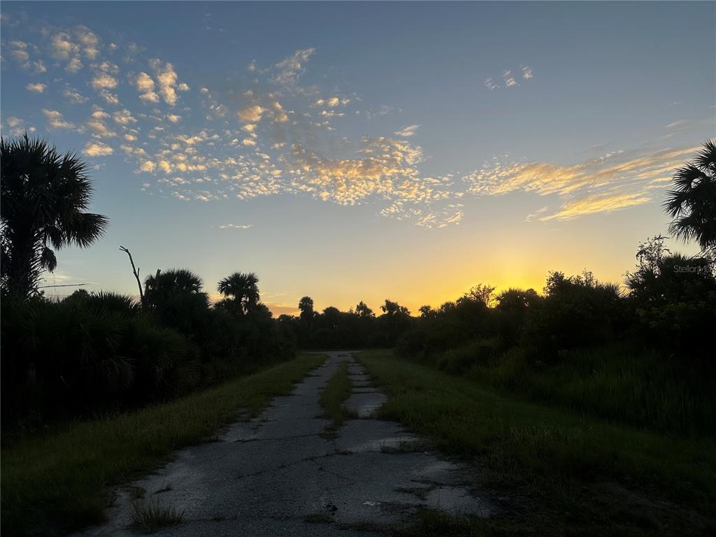 A paved path leads through a grassy, wooded area toward a sunset on the horizon — DUNE COURT, NORTH PORT, FL