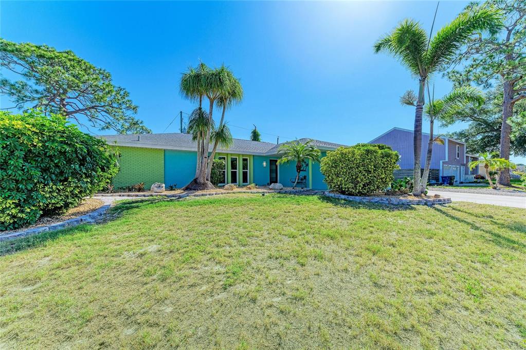 A single-story house with a turquoise and lime green exterior sits behind a grassy lawn — 1184 KENISCO ROAD, VENICE, FL