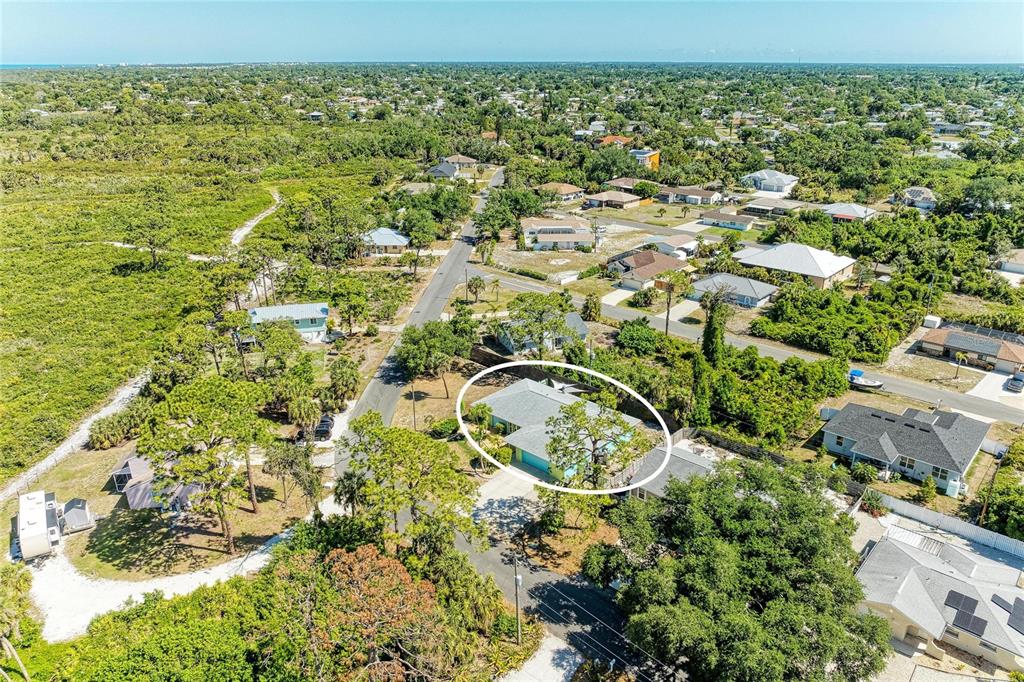 An aerial view shows a single-story house with a gray roof surrounded by lush vegetation — 1184 KENISCO ROAD, VENICE, FL