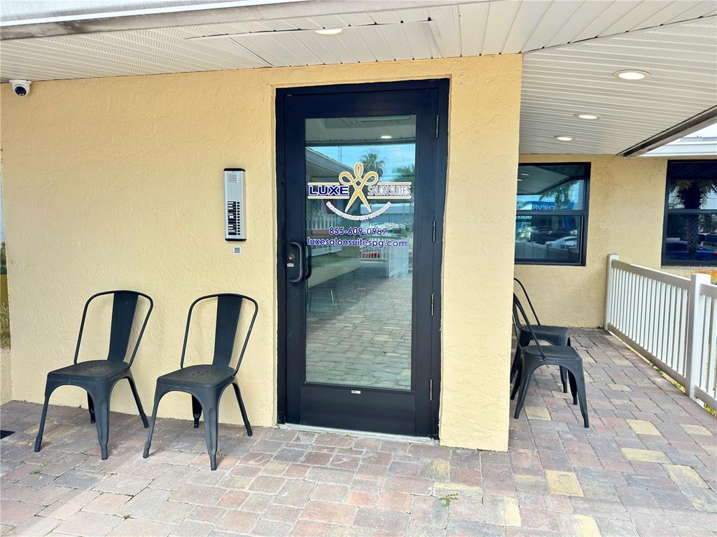A black glass door with signage sits between two pairs of black metal chairs outdoors — 1900 TAMIAMI TRAIL UNIT C & D, PUNTA GORDA, FL