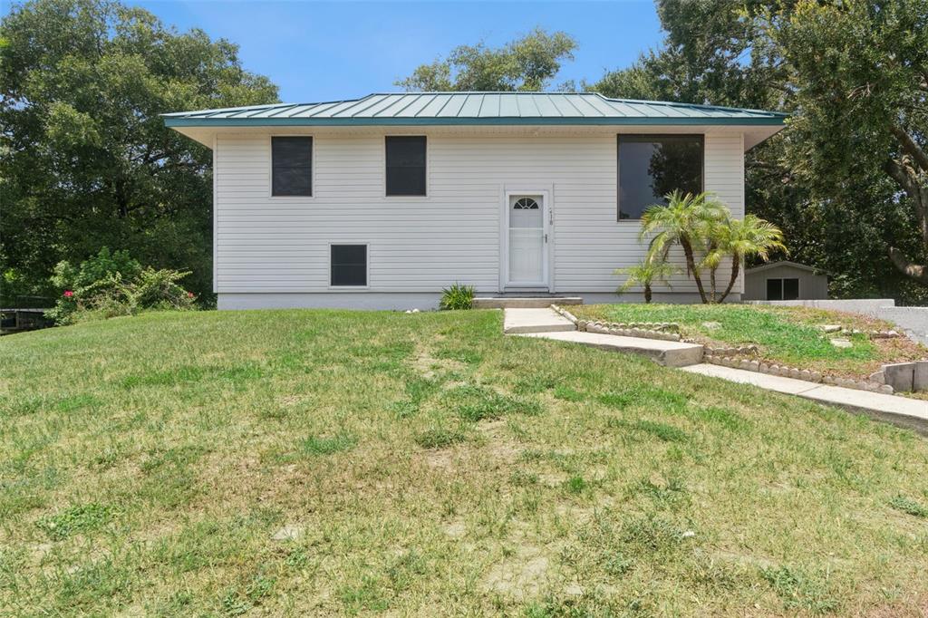 A single-story house with white siding and a green metal roof sits on a hill — 218 LAVENDER COURT, ORLANDO, FL