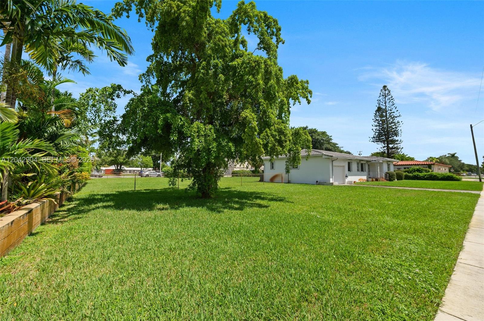 A large grassy yard features a mature tree and a white house with a garage — 20 SW 4th St, Dania Beach FL 33004, DANIA BEACH, FL
