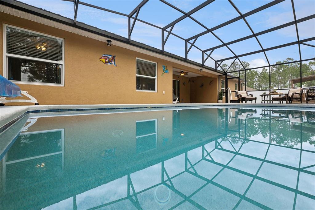 A swimming pool with a screened-in enclosure sits beside a tan house with windows — 68 KATHLEEN TRAIL, PALM COAST, FL