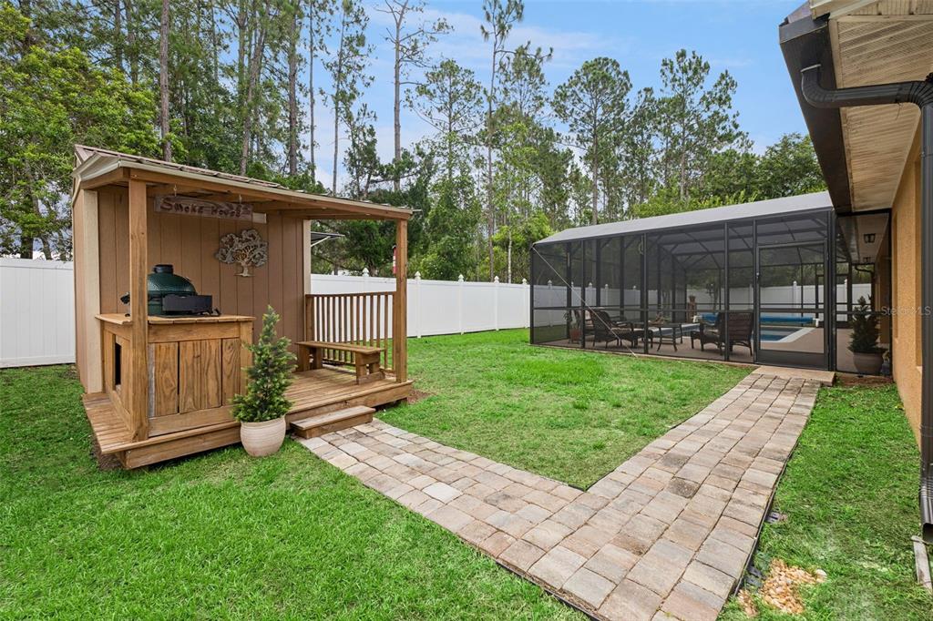 A backyard features a wooden smokehouse structure, a paver walkway, and a screened-in pool enclosure — 68 KATHLEEN TRAIL, PALM COAST, FL