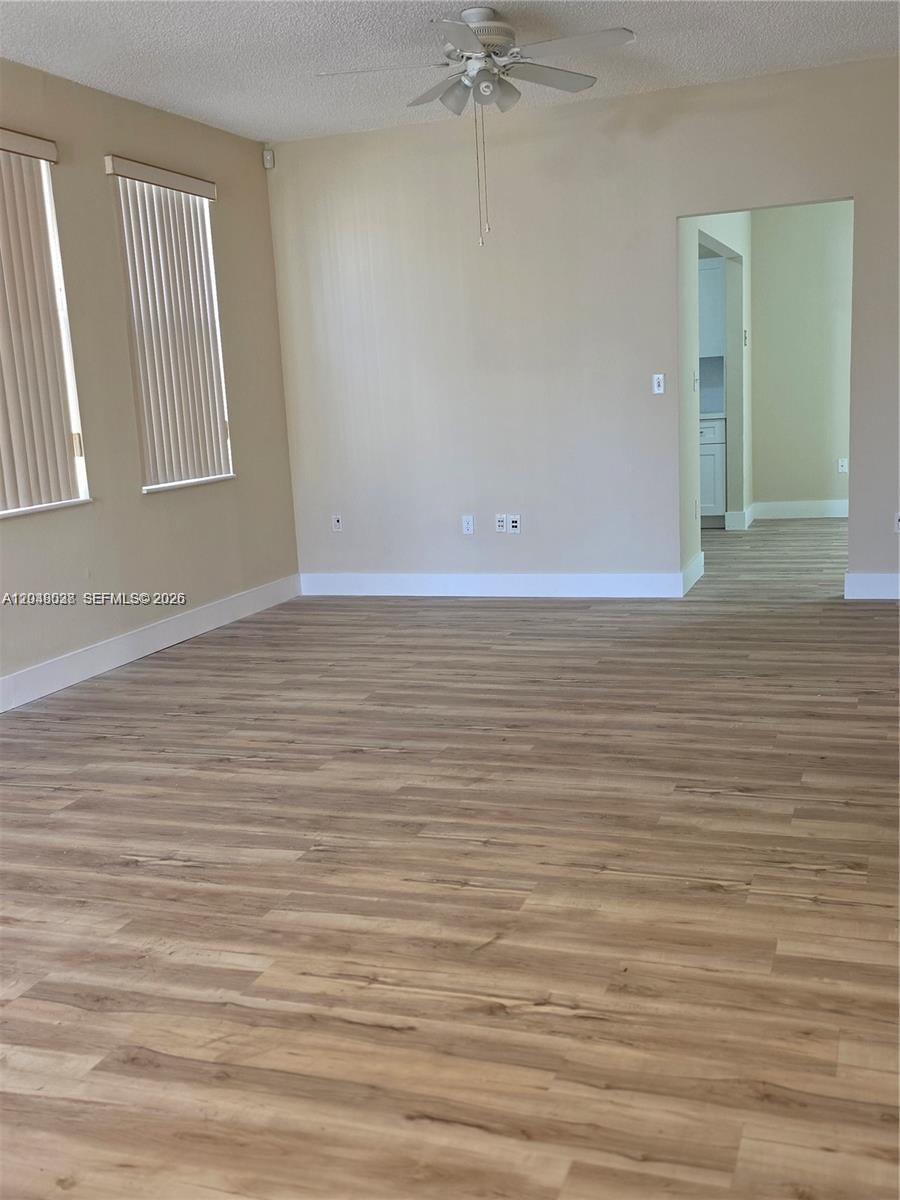 An empty room features light wood-look flooring, beige walls, two windows, and a ceiling fan — 2926 SW 26 ST, Miami FL 33133, MIAMI, FL
