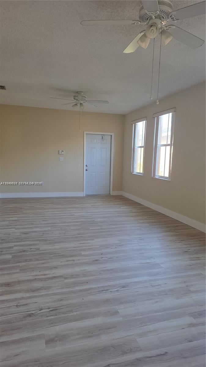An empty room features light-colored wood-look flooring, beige walls, two ceiling fans, and a door — 2926 SW 26 ST, Miami FL 33133, MIAMI, FL