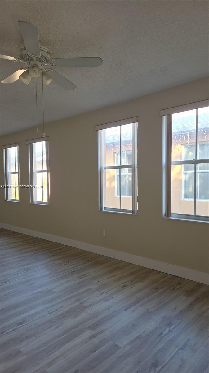 An empty room features light wood-look flooring, beige walls, a ceiling fan, and four windows — 2926 SW 26 ST, Miami FL 33133, MIAMI, FL