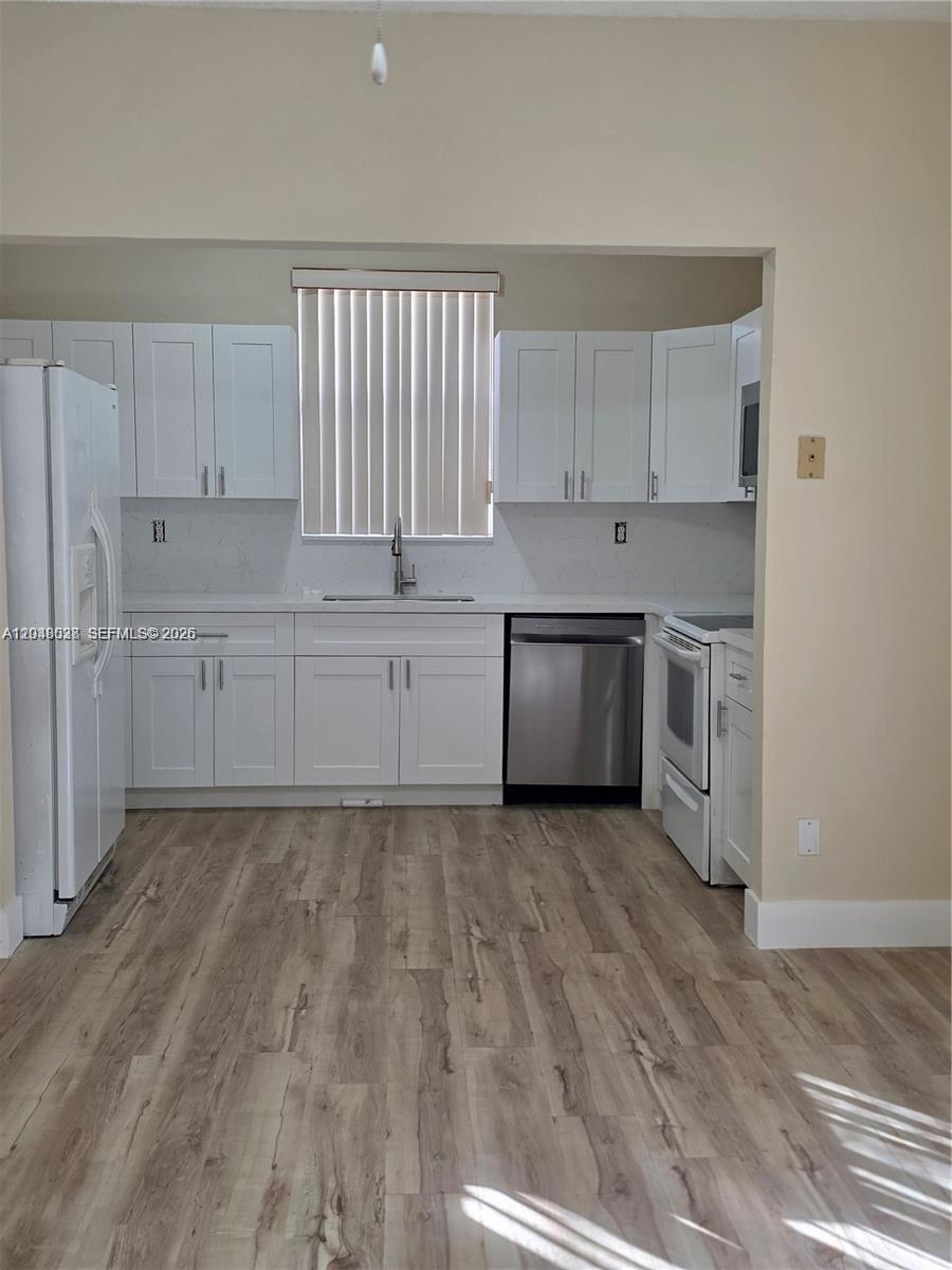 A kitchen features white cabinets, stainless steel appliances, a window, and light wood-look flooring — 2926 SW 26 ST, Miami FL 33133, MIAMI, FL