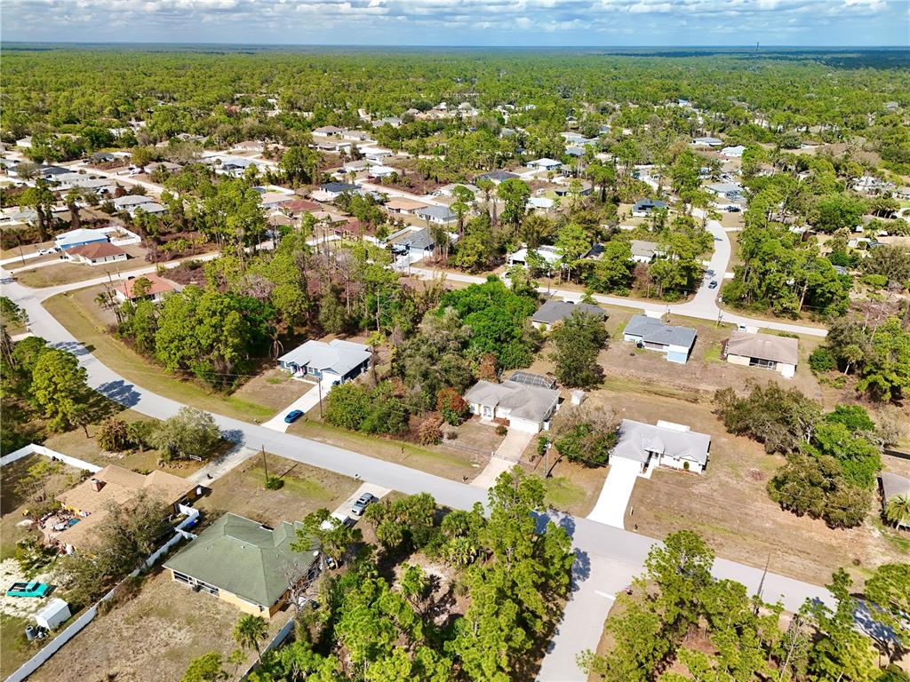 An aerial view shows a suburban neighborhood with single-family homes surrounded by dense green trees — MERONI BOULEVARD, NORTH PORT, FL