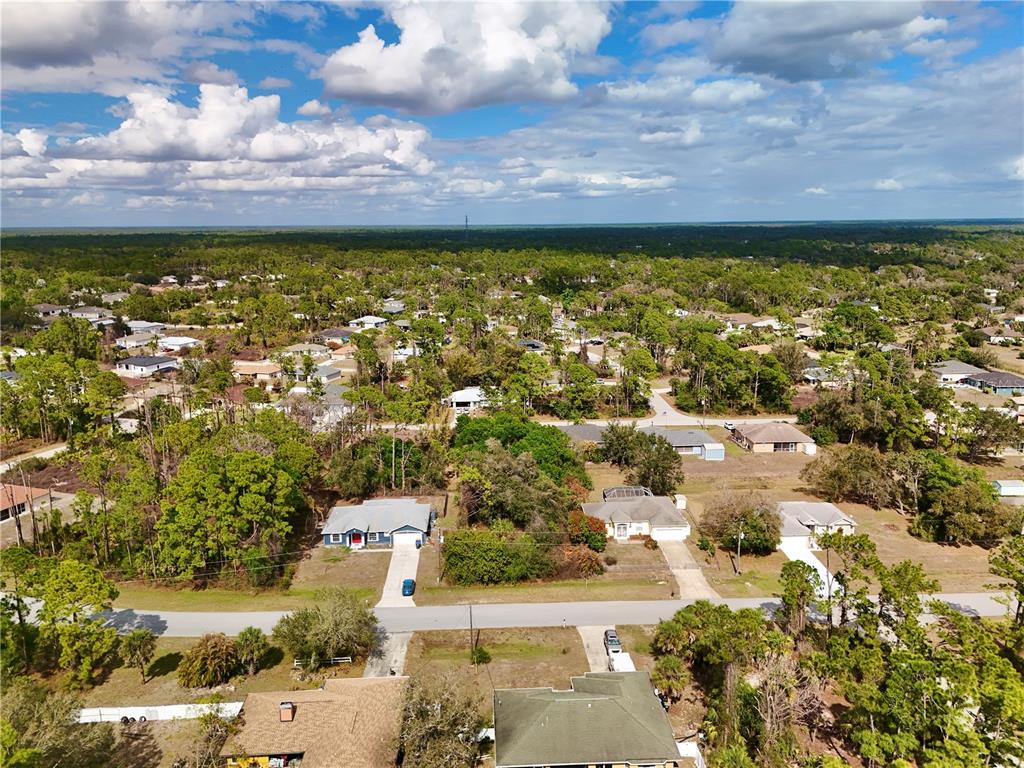 An aerial view shows a suburban neighborhood with houses, trees, and roads under a cloudy sky — MERONI BOULEVARD, NORTH PORT, FL