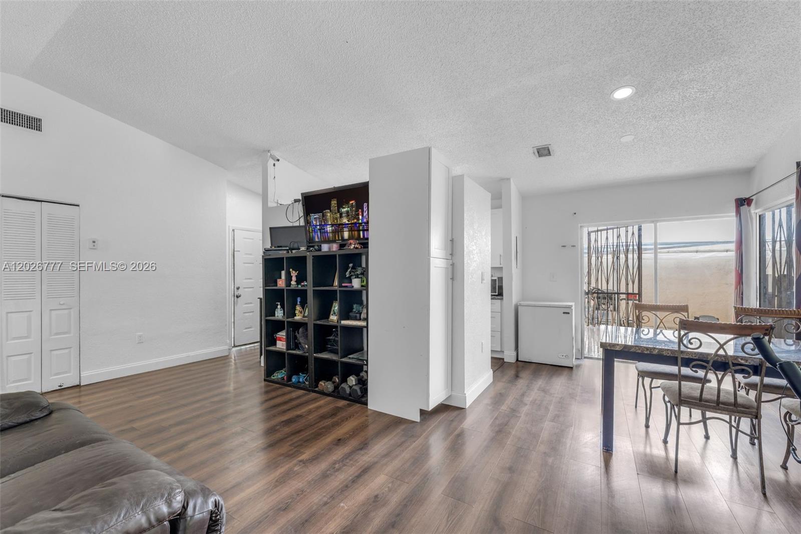 This living and dining area features wood-look flooring, a central shelving unit, and sliding doors — 12026 SW 210th St, Miami FL 33177, MIAMI, FL
