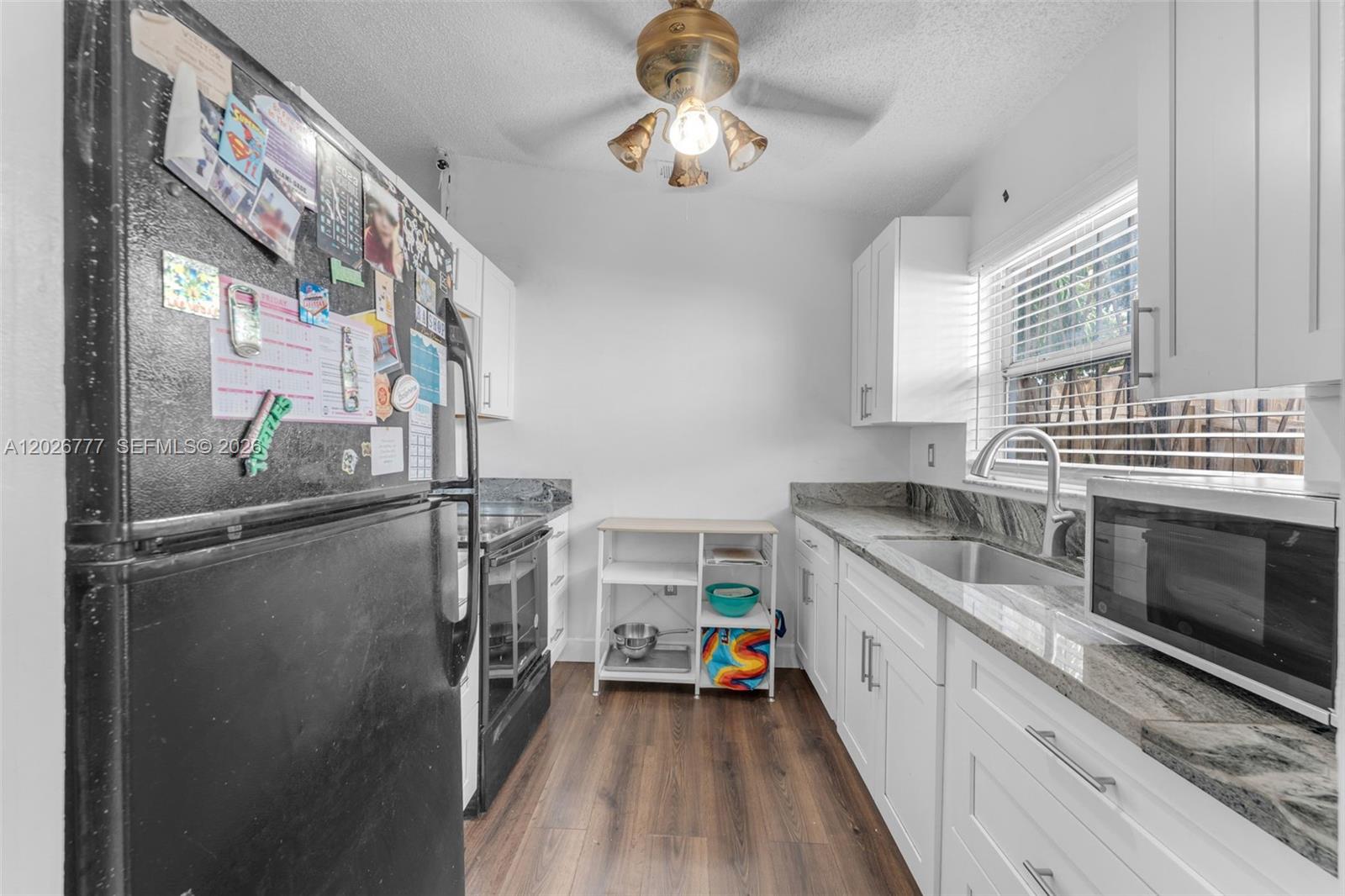 A galley kitchen features white cabinets, granite countertops, stainless steel appliances, and wood-look flooring — 12026 SW 210th St, Miami FL 33177, MIAMI, FL